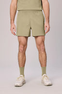 Men's light olive green athletic shorts with elastic waistband, paired with matching socks and white sneakers