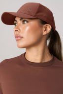 Woman wearing a sepia brown athletic cap and matching crew neck top, side profile view