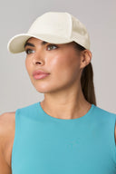 Woman wearing a white athletic cap and light blue sleeveless top, minimal background