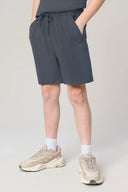 Boy wearing granite gray athletic shorts with pockets, sneakers, and white socks standing indoors