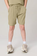 Boy wearing willow green athletic shorts with elastic waistband and drawstring, sporty sneakers