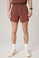 Man wearing sepia brown athletic shorts, white socks, and sneakers on neutral background