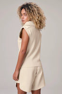Woman modeling beige sleeveless vest and shorts athleisure set, back view