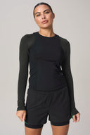 Woman wearing charcoal long sleeve athletic tee and black active shorts, neutral background