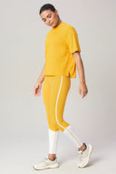 Woman wearing spicy mustard yellow loose fit short sleeve athletic top and matching leggings with white accents, standing in a studio setting