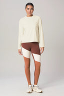 Woman wearing loose fit cream long sleeve top with colorblock brown and beige leggings, athleisure style