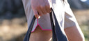 Close-up of beige athletic shorts with neon trim, person holding black strap outdoors