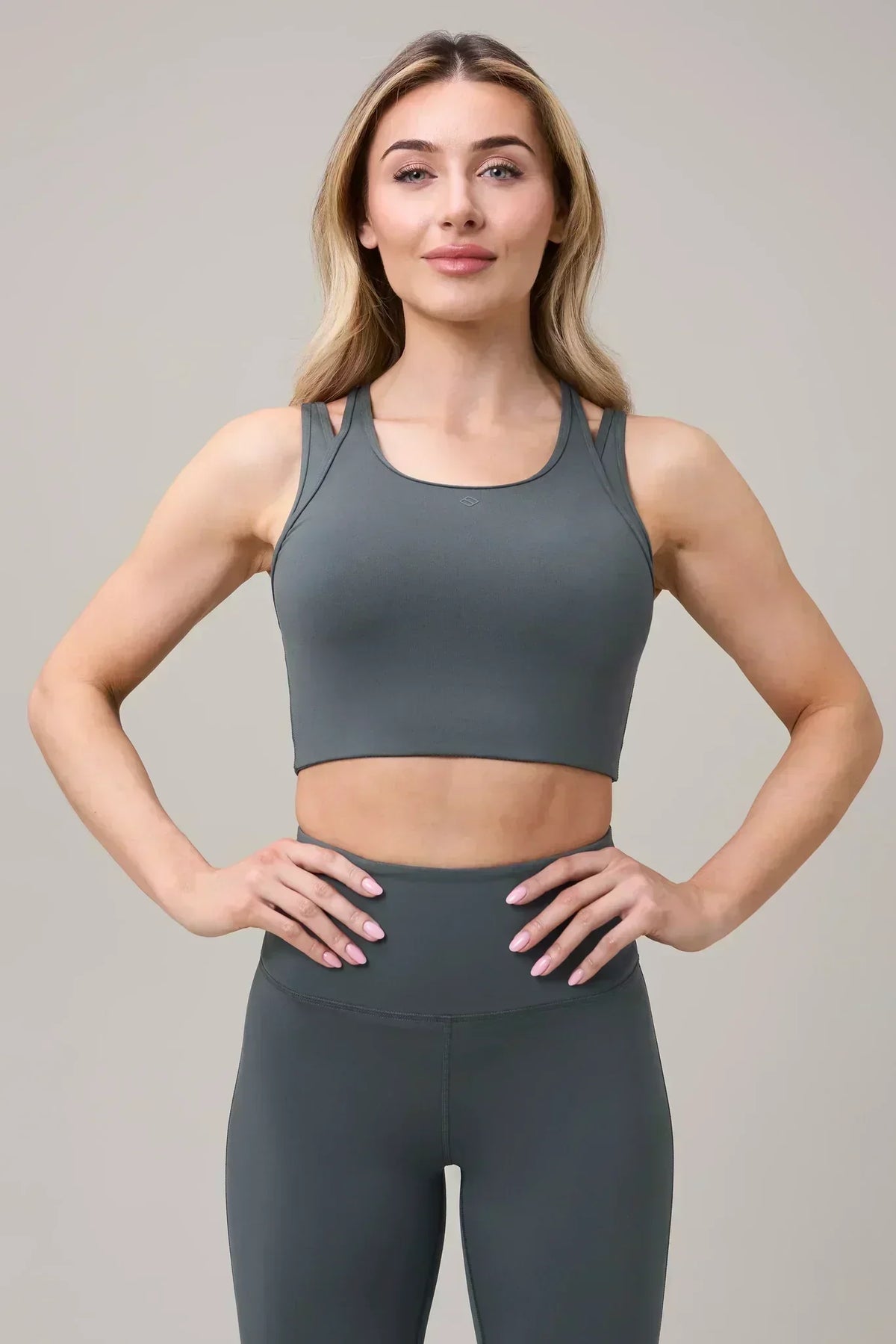 Woman wearing grey athleisure sports bra and high-waisted leggings, hands on hips