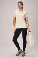 Woman in sand beige performance tee and black leggings holding matching towel, activewear