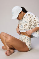 Woman in floral print athleisure crop top and high-waist shorts, wearing a light cap, sitting