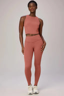 Woman wearing burnt amber high-neck compression bra and matching leggings, white sneakers