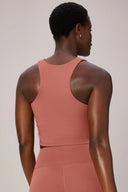 Woman wearing a burnt amber racerback sports bra and high-waisted leggings, back view