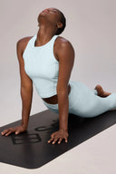 Woman practicing yoga in light blue cropped tank and leggings on black mat