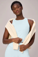 Woman in light blue compression sports bra and leggings with cream sweatshirt over shoulders