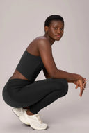 Woman in charcoal mesh compression bra and textured leggings, squatting, white sneakers