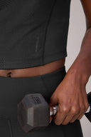 Close-up of a person in a textured charcoal compression sports bra and leggings holding a dumbbell