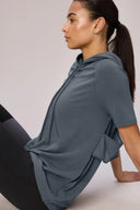 Woman in granite gray short sleeve Pima hoodie with mesh pocket, seated, side view