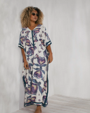 Woman in a loose floral kaftan dress with purple and teal patterns, standing indoors