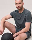 Man in dark grey athletic t-shirt and shorts sits with an exercise ball, activewear shoot