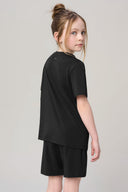 Girl in charcoal short sleeve tee and shorts, looking back, plain background