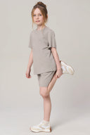 Girl in neutral driftwood tee and shorts athleisure set, stretching, white background