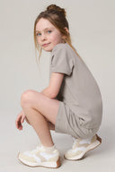 Young girl in a driftwood beige t-shirt and shorts set with white sneakers, neutral background