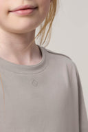 Close-up of girl wearing driftwood beige basic tee, minimalist logo, soft fabric