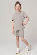 Girl wearing neutral driftwood basic tee and shorts athleisure set, white sneakers