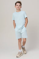 Boy wearing light blue athletic t-shirt and shorts set with sneakers on plain background