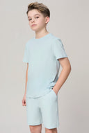 Boy wearing light blue short sleeve athleisure tee and shorts set against plain background