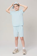 Boy wearing light blue athletic t-shirt, matching shorts, and sneakers, holding a cap