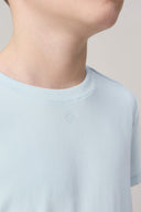 Close-up of a child wearing a light blue short sleeve crewneck t-shirt with a subtle chest logo