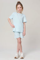 Girl wearing light blue short-sleeve athleisure tee and shorts set, standing in studio