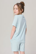 Girl wearing light blue short sleeve athleisure set, standing in profile, neutral background