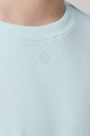 Close-up of a light blue crewneck tee with subtle chest logo, soft athleisure fabric