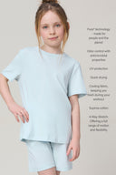 Girl wearing light blue short-sleeve athleisure tee and shorts, neutral background.