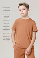 Boy wearing mocha short-sleeve tee and pants, features listed: odor control, UV protection, stretch.