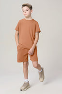 Boy wearing mocha brown athletic t-shirt and shorts set, posing in neutral studio