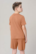 Boy wearing mocha brown short sleeve tee and matching shorts, facing away, plain background