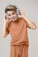 Smiling boy wearing a mocha brown basic tee and headphones, neutral background