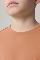 Close-up of boy wearing mocha brown basic tee with crew neck and small chest logo