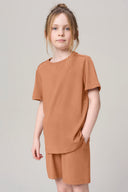 Girl wearing mocha brown basic short-sleeve tee and shorts, neutral background.