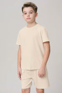 Boy wearing sand beige short sleeve tee and matching shorts, neutral studio background