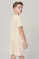 Boy in sand-colored short sleeve tee and shorts, side view, neutral background