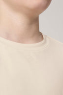 Close-up of a boy wearing a sand beige basic tee with subtle chest logo