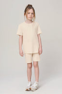 Girl wearing sand-colored basic tee and matching shorts, white sneakers, neutral background