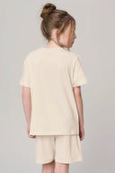 Girl wearing sand beige short-sleeve tee and matching shorts, shown from the back