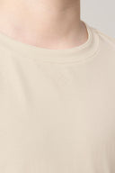 Close-up of a beige crew neck t-shirt with a small minimalist logo on the chest.