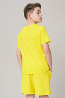 Boy wearing bright yellow short-sleeve tee and matching shorts, back view, neutral background