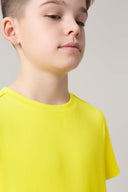 Boy wearing a bright yellow short sleeve tee with minimal design in a neutral setting
